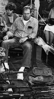 Eugene Hasenfus sits among the weapons captured from his downed cargo plane. His Sandinista captors surround him.