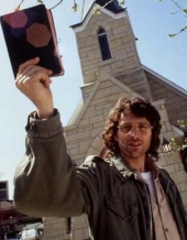 David Koresh holds up a Bible while standing in front of a church.
