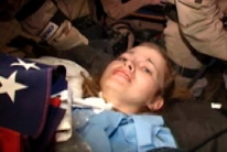 A barely conscious Lynch lies on a stretcher. An American flag is draped over her chest. This will become one of the iconic photos of the Lynch saga.